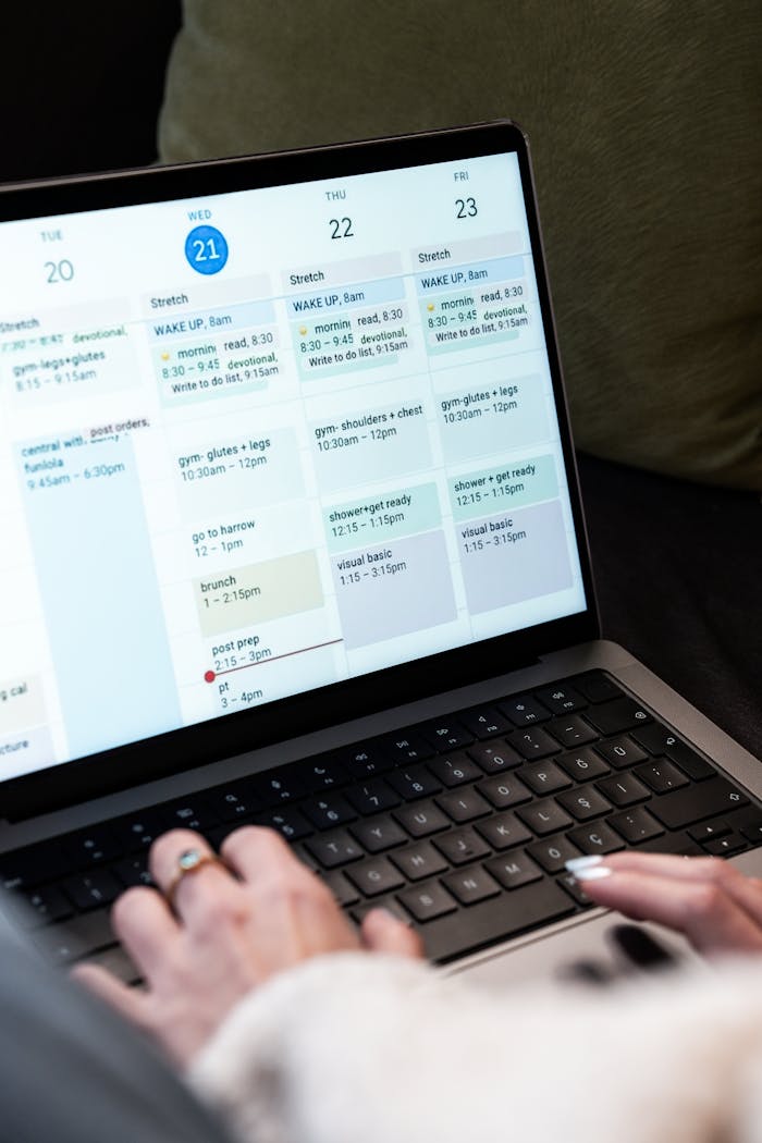 A woman types on a laptop while planning her weekly schedule using a digital calendar.