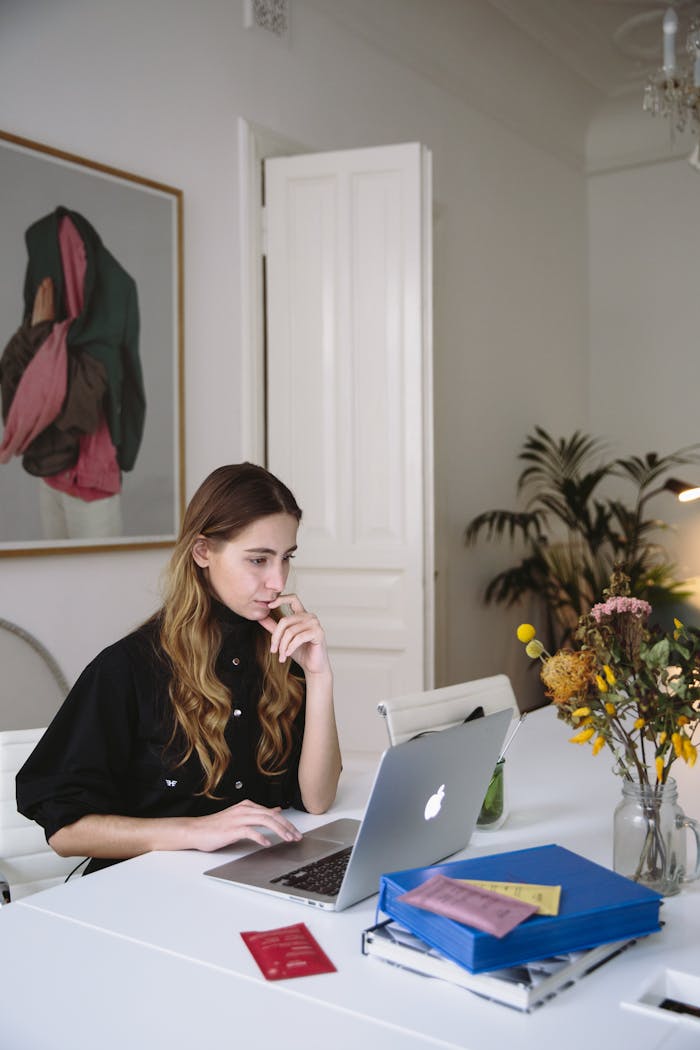 Woman working on a laptop at home, embracing digital nomad lifestyle. Modern workspace with plants.